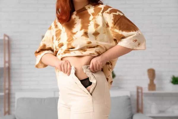 Image of woman trying to do her trousers up after pregnancy weight gain Maidenhead